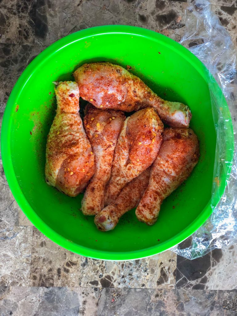 Chicken Drumsticks in a green mixing bowl with cajun seasoning, paprika and red pepper flakes sprinkled all over them.
