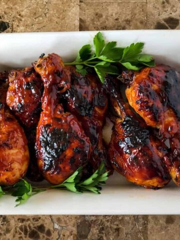 Chicken drumsticks covered in BBQ sauce in a white serving platter garnished with parsley.