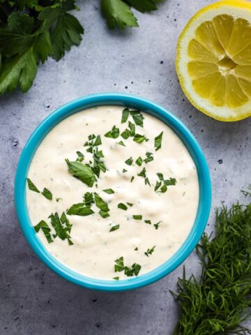 Tartar sauce in aqua bowl garnished with chopped parsley.