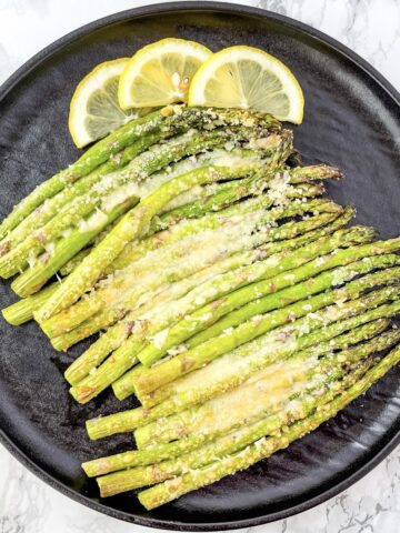 Plate of asparagus topped with melted parmesan cheese garnished with lemon slices.